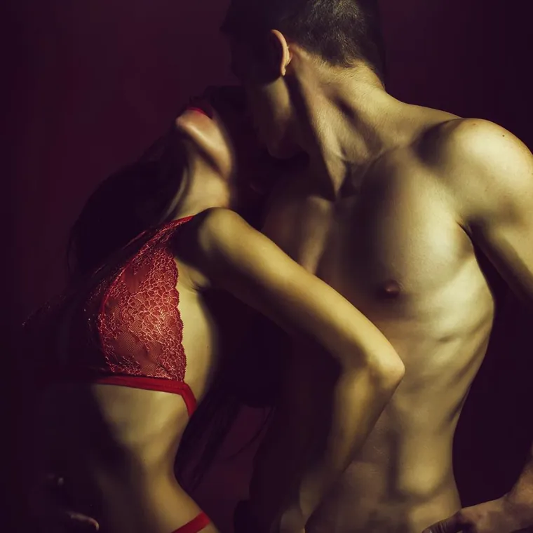 A woman in red lace lingerie leans back as a shirtless man kisses her neck